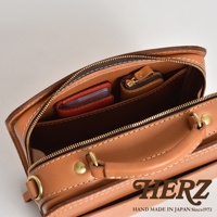 職人手作皮革兩用方形單肩包，皮革為棕色，配有金色拉鍊和扣環，內部可見紅色卡夾和一個小皮質收納包。