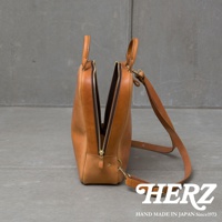 職人手作皮革Organ商務後背包，以自然光照亮，展示其精緻的縫線和金屬拉鍊細節，皮革呈現溫潤的棕色調。