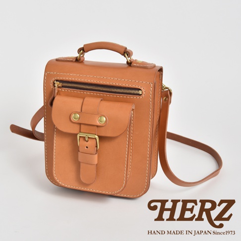 職人手作淺棕色皮革立體口袋兩用單肩包，帶有黃銅釦環和拉鍊，以及可調整的肩帶。