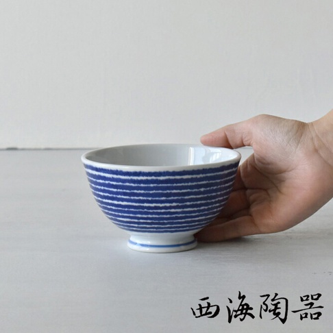 一只手正拿著一個波佐見燒藍玉紋飯碗，碗身有細緻的藍色橫紋，碗底有藍色圈紋，碗內為白色。
