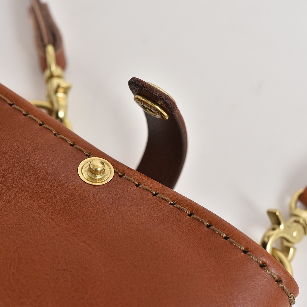 職人手作皮革兩用手機包，採用棕色皮革，搭配黃銅色金屬扣環與鉤鍊，縫線工藝精緻，展現質感。