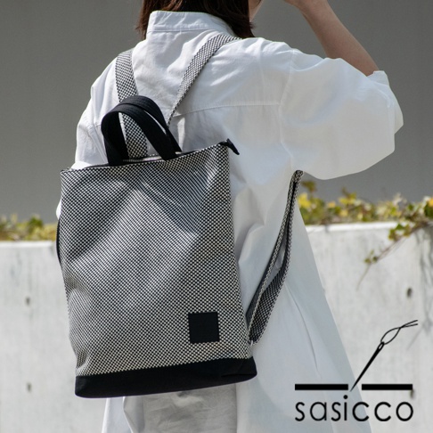 黑白格紋刺子織手提後背包，配有黑色提把與肩帶，底部為黑色純色拼接。