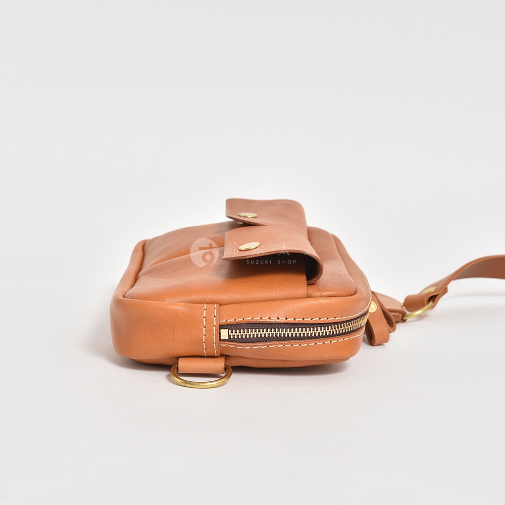 職人手作皮革雙口袋斜背包 F-10，採用棕色皮革製成，設有黃銅色按扣和拉鍊，配有可調節的皮革背帶。