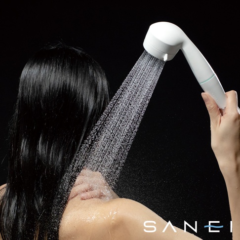 MIGAMI 兩段式水流專髮按摩蓮蓬頭，白色圓潤造型，搭配淺綠色飾帶。手持蓮蓬頭，水流從圓形噴頭灑出，淋在一位擁有烏黑長髮的女性的頭部與肩頸。