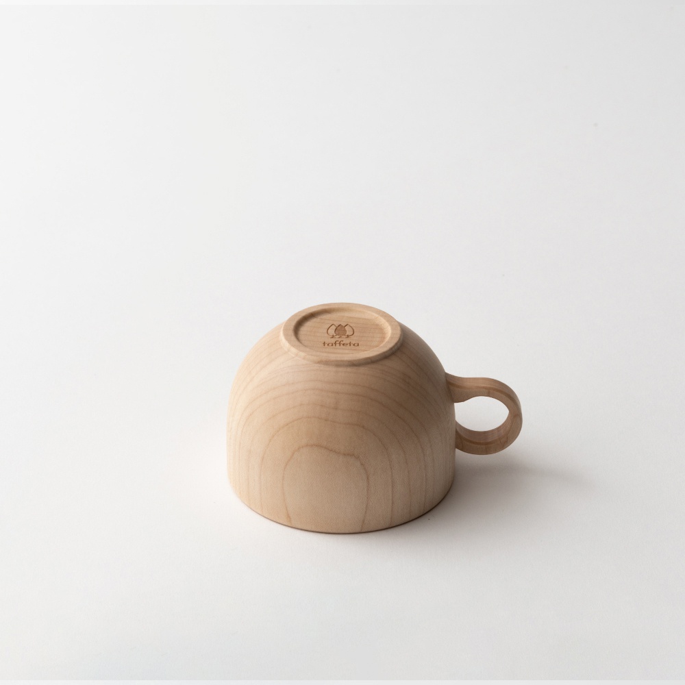 淺色楓木茶杯，杯底朝上，露出品牌標誌，帶有圓形手柄，木紋清晰自然。