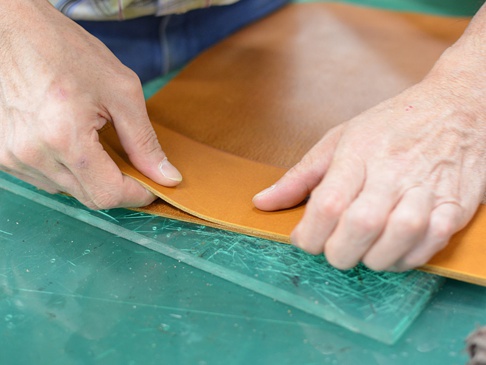 一雙手正在操作牛皮紙，準備製作A4筆記本書套。牛皮紙呈現自然的淺棕色，質感細膩。