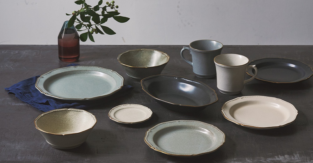 Aito Stitch 系列復古陶器，包含帶有金邊浮雕的淺藍色和淺黃色湯碗、橢圓形深灰色烤盤、灰藍色和米白色馬克杯，以及一個深灰色盤子。