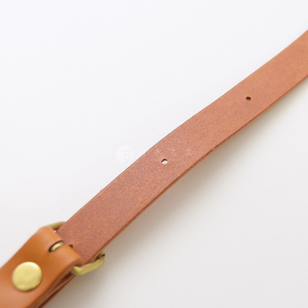 一張特寫照片，展示了職人手作皮革肩背帶的細節，包括縫線、黃銅扣環和皮革的紋理。