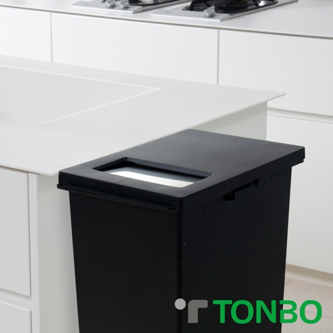 黑色雙層雙用型分類垃圾桶，帶有可放入垃圾的長方形開口，置於白色廚櫃旁的角落。