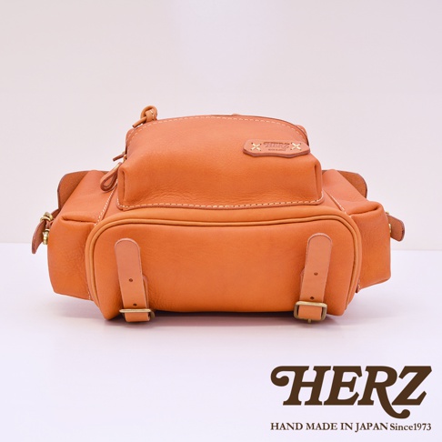 職人手作皮革復古風旅行後背包，橘棕色皮革，雙層設計，前袋有兩條帶扣，側邊有提把，金屬拉鍊及扣環。
