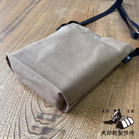 淺色帆布平板收納側背包，附黑色背帶，放置於木紋桌面。