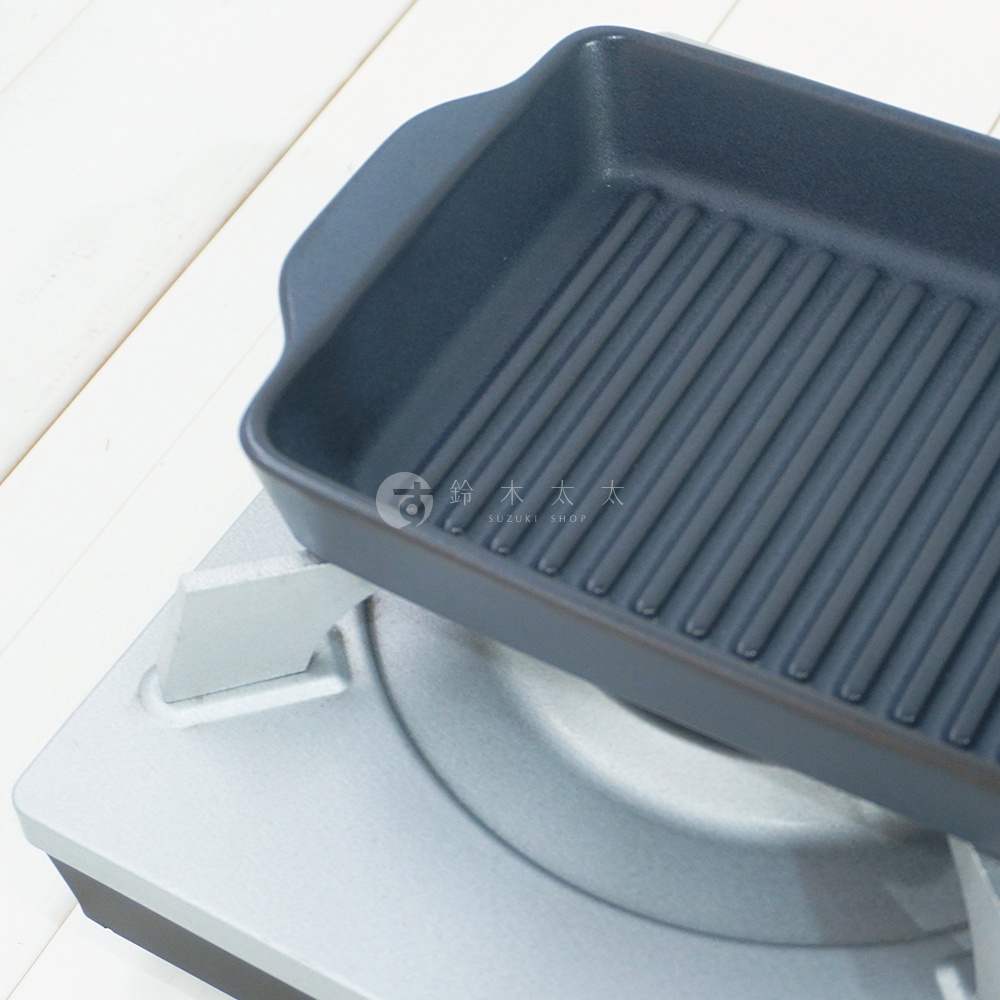 深灰色陶製長方形烤盤，內部設有條狀紋路，烤盤邊緣有兩個把手，置於銀色爐架上。