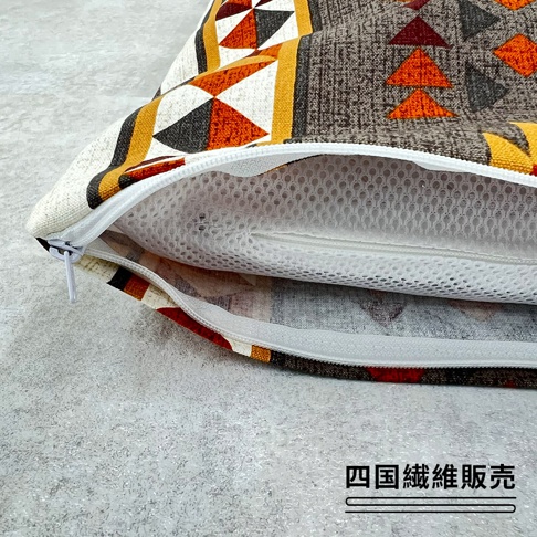 一個具有民族風圖騰的枕頭套正呈現開啟狀態，露出內部帶有細小孔洞的白色透氣網狀枕芯，右下角印有四國纖維販賣的品牌標示。