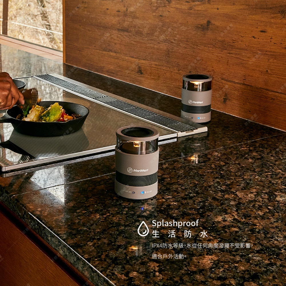 兩個圓柱形氛圍燈音響，一個在前景，一個在背景，皆為灰褐色，帶有銀色飾條與網狀底部。頂部有燈光，側面印有「MoriMori」標誌。