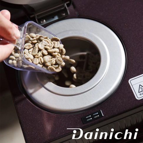 淺綠色咖啡生豆從透明勺子倒入深棕色自動生豆烘焙咖啡機 MC-520A 的烘焙槽中。