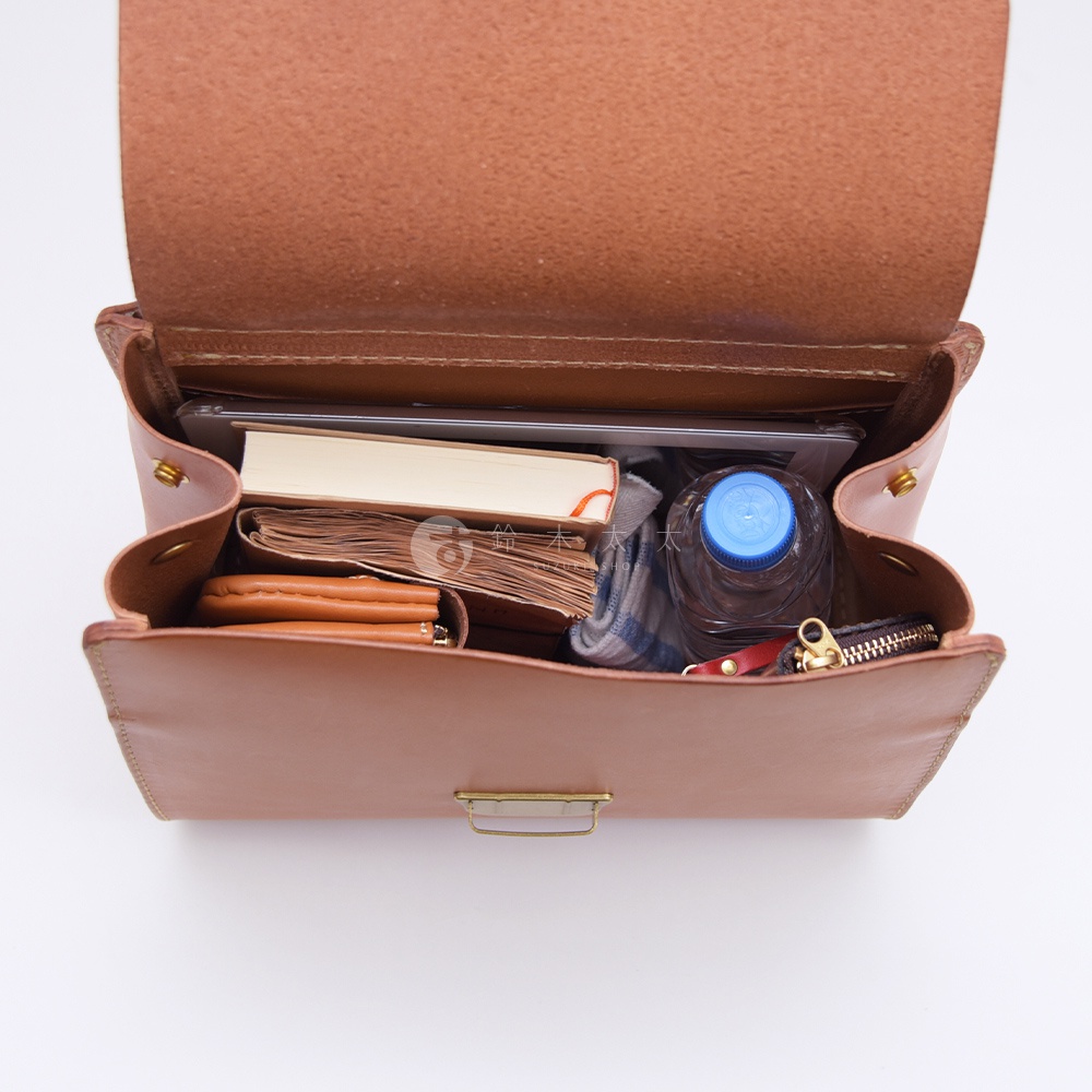 一款棕色皮革包，裡面裝有書本、水瓶和錢包。