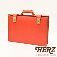 職人手作皮革機師箱 BC-31，橘紅色皮革，設有兩個金色鎖扣和一個提把，箱體邊緣有縫線裝飾。