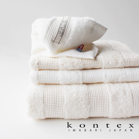 堆疊的白色今治雙織有機棉浴巾，頂部浴巾上有「Organic cotton 100%」標籤。浴巾呈現鬆餅格紋織紋，質地柔軟。