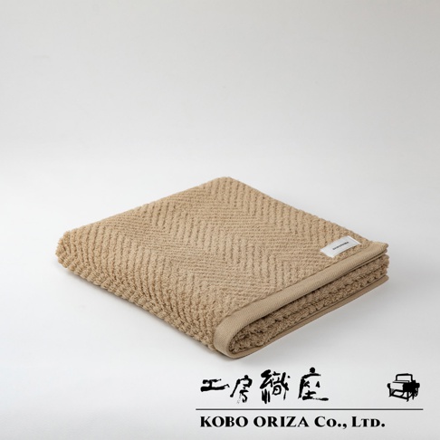 ECOR 天然系人字紋有機棉浴巾，呈現溫暖的米褐色，織有經典人字紋路，質感柔軟。