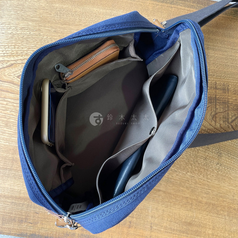 藍色石洗帆布旅行側背包內部，可看到手機、錢包及筆，還有多個隔層方便收納。