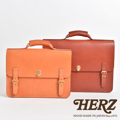 兩款皮革公事包，一款為淺棕色，另一款為深棕色，皆配有頂部提把、金屬鎖扣和雙皮帶扣。