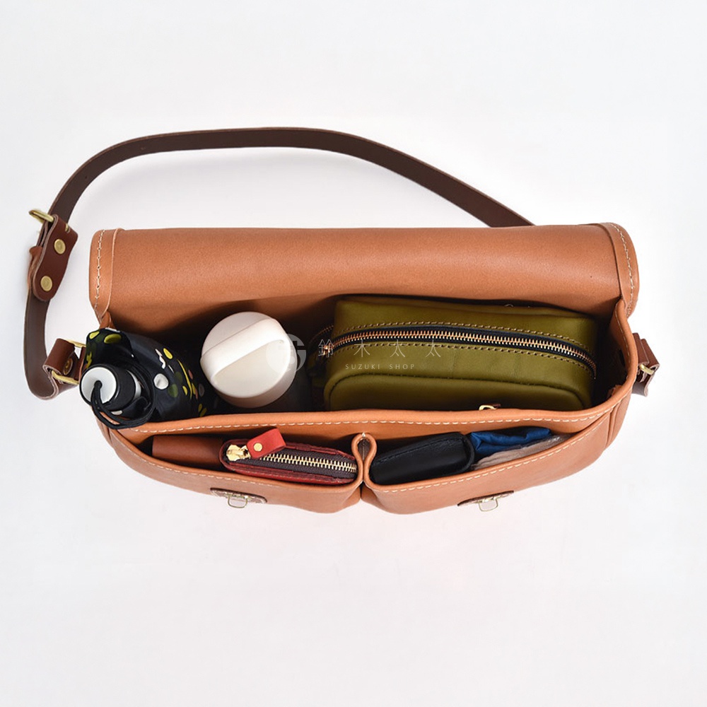 職人手作皮革傳統釣魚包CK-21，展示其內部配置。包身為棕褐色皮革，內有綠色化妝包、白色圓形物品、黑色與黃色斑點摺疊傘，以及紅色與黑色的零錢包。