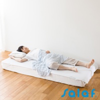 一名男子仰臥在白色單人睡墊上，蓋著藍白色條紋毛毯，頭枕在白色枕頭上。睡墊為白色，邊緣有淺藍色滾邊。