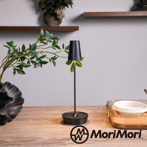 黑色金屬復古氛圍燈，圓形底座，細長燈柱，錐形燈罩，散發溫暖光線，旁有綠葉裝飾。