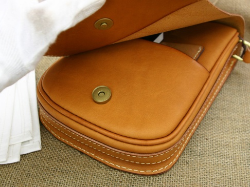 職人手作皮革翻蓋直式單肩包，採用棕褐色皮革製成，包身線條簡潔，翻蓋處有金色磁釦，縫線清晰。