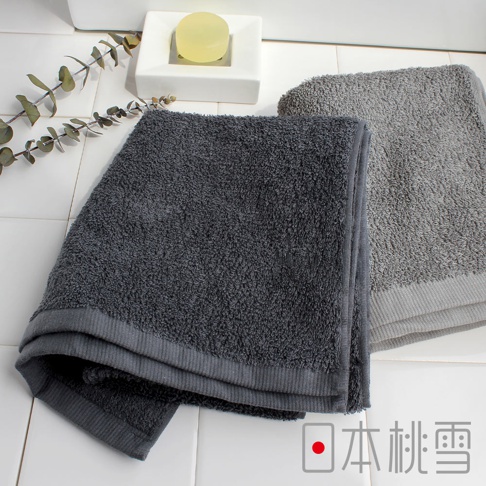 日本桃雪的深灰色和淺灰色厚毛巾，搭配白色瓷磚背景和一塊黃色香皂。