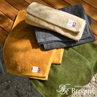 黃色、灰色、卡其色和綠色的今治純棉毛巾，部分疊放於木桌上，毛巾上有品牌標籤。