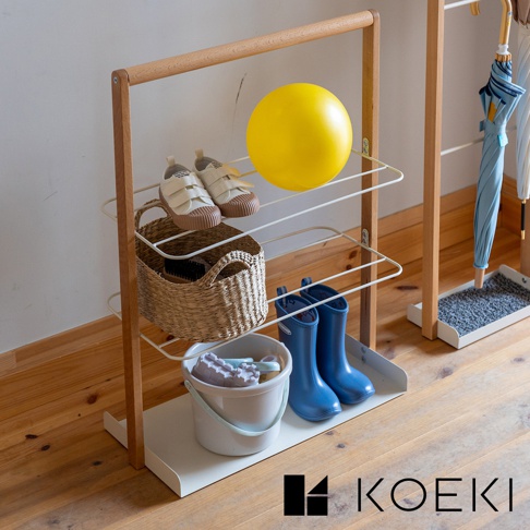 木質框架搭配白色線條層架的鞋靴收納架，架上擺放著一雙白色帆布鞋、一個草編籃、藍色雨靴、一個白色水桶及玩具，以及一個黃色圓球。