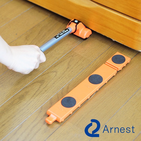 橘色長型迷你家具起重器，帶有銀灰色金屬手柄，正被用於抬起木質家具的底部。另一相同材質的橘色起重器平放在木質地板上，上面有黑色防滑墊和刻度標示。