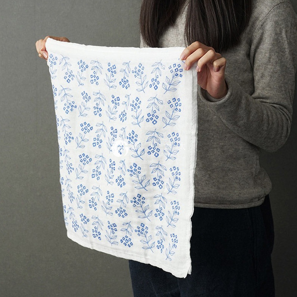 純棉花草紗布大拭巾，白色底布上印有藍色細緻的花草圖案，質地輕柔。