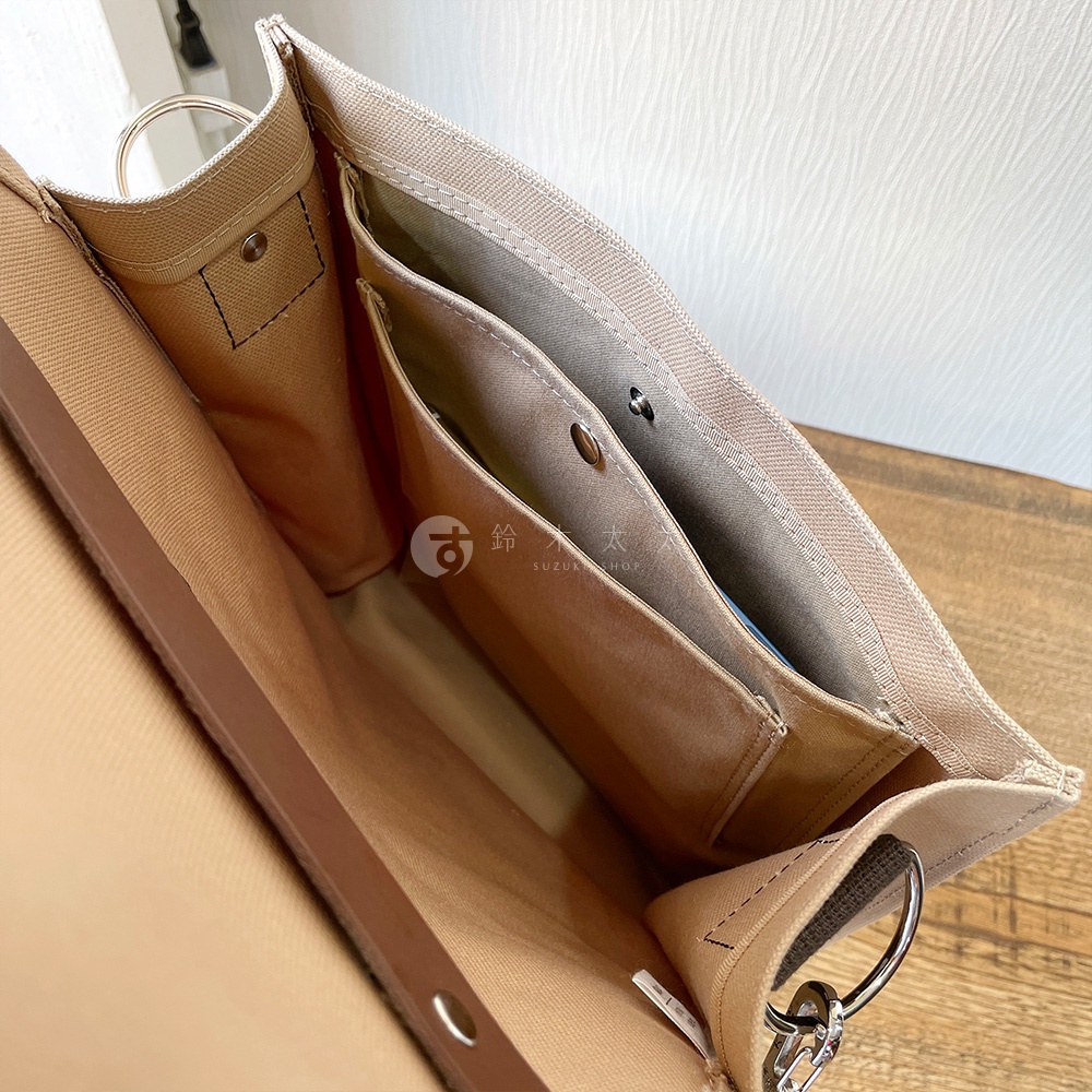 犬印純綿帆布三用直式側背包，米白色帆布材質，內部有多個隔層，包含兩個開放式口袋和一個帶有金屬釦的口袋，側邊有 D 型環，整體設計簡潔實用。