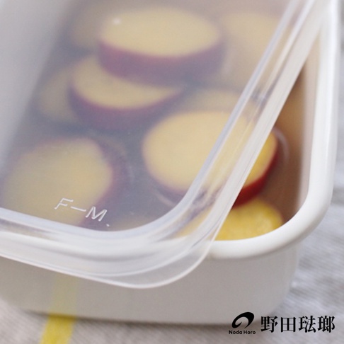 長方型淺型白色琺瑯保存容器，內部裝有切片的黃色食材，容器蓋為透明塑膠材質，上面印有「F-M.」字樣。