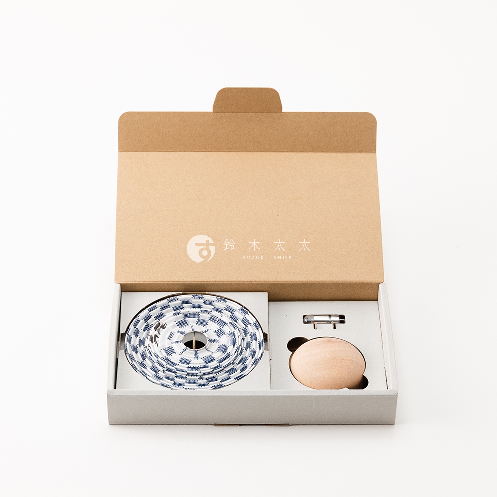 打開的紙盒內，左側為藍白色棋盤格紋的圓形繩結，右側為木製達摩不倒翁和金屬零件。