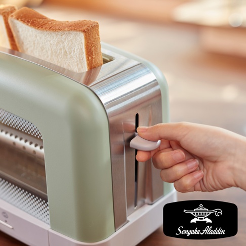 淺綠色烤麵包機，配有銀色金屬飾邊。兩片金黃色的烤吐司插在槽中。一隻手正在操作銀色控制桿。