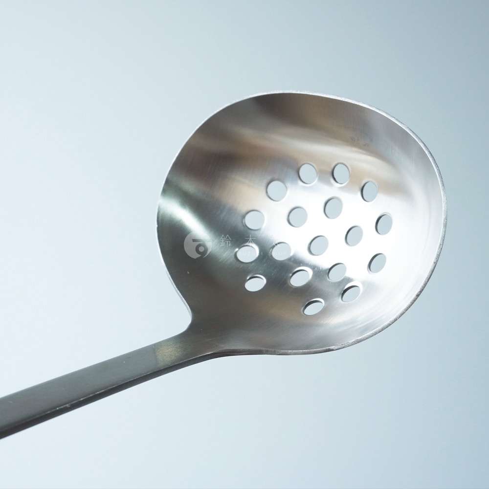 不鏽鋼萬用瀝水湯勺，勺面呈圓弧形，佈滿圓形瀝水孔，手柄為長條狀，整體為銀色金屬質感。