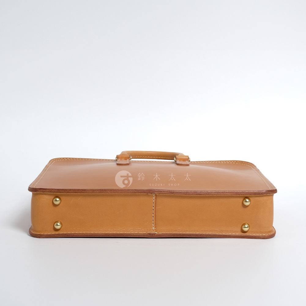 職人手作皮革手提商務公事包，天然皮革材質，焦糖色，配有頂部提把及金屬卯釘裝飾，設計簡潔大方。