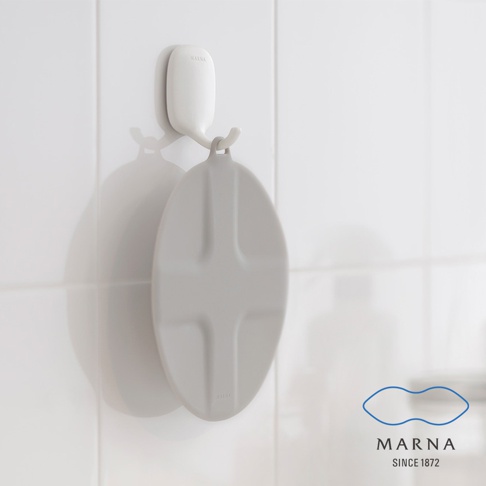 一個灰色的圓形矽膠水槽蓋，上面有十字凹槽設計，掛在白色牆面上的白色掛鉤上。