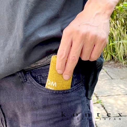 一條黃色MOKU超速乾輕薄吸水小方巾，織紋清晰，一角露出「OM」字樣，被放入深藍色牛仔褲的口袋中。