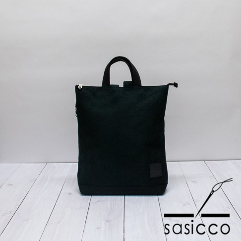 深綠色三河木綿刺子織手提後背包，織紋清晰，設有拉鍊開合及雙提把，右下方有同色系方形品牌標籤。