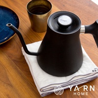 白色廚房拭巾，帶有灰色滾邊，上面放著一個黑色細嘴咖啡壺，壺蓋上裝有溫度計。