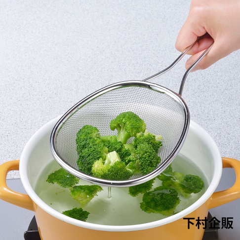 不鏽鋼橢圓濾網，網目細緻，盛有綠色花椰菜，上方有手持濾網，濾網下方為裝有水的黃色鍋子。