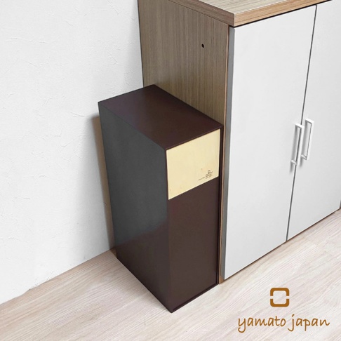 深棕色前開式隙縫可堆疊垃圾桶，上方有淺木色面板，旁邊為白色雙門櫃。