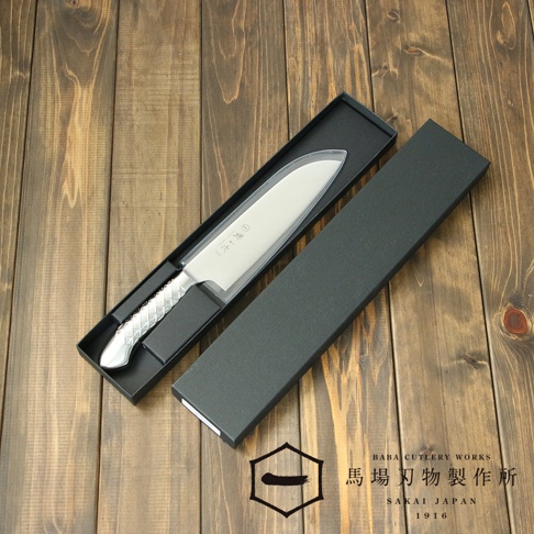 [堺一次] 不鏽鋼三德刀，刀刃呈銀白色，握柄為菱形紋理的銀色不鏽鋼，置於黑色長方形禮盒內，背景為木紋桌面。