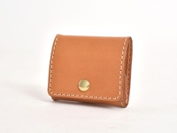 職人手作的淺棕色皮革箱型零錢包，正面有一個金色圓形按扣，採用白色車線縫製，呈現簡潔俐落的設計。