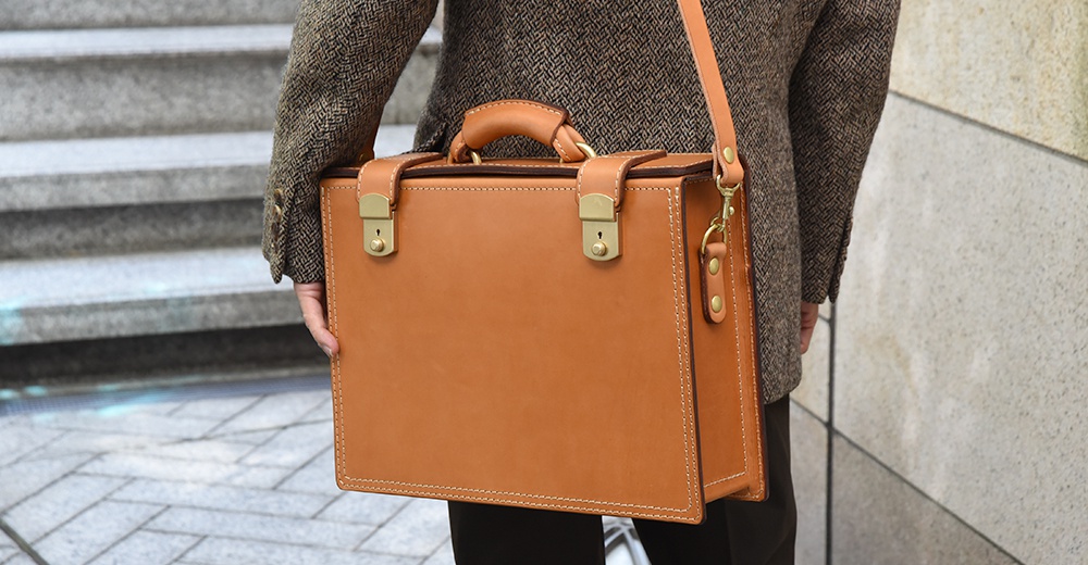 職人手作皮革兩用機師箱，採用原色皮革製作，配有金色鎖扣和提把，可肩背或手提。