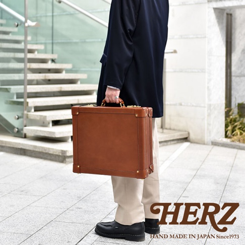 職人手作皮革英倫風便攜手提行李箱，採用鞣製皮革材質，呈現自然棕色調。箱體方正，搭配金色金屬鎖扣與提把，側面有加固金屬角釘，整體風格簡約大方。